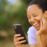 A woman laughing while checking her phone after receiving Love & Trust Messages for Long-Distance Relationships For Her.
