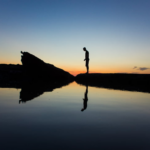 Person standing in silence by a calm lake at sunset, demonstrating The Secret Psychology of Saying Nothing