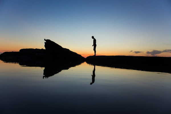 Person standing in silence by a calm lake at sunset, demonstrating The Secret Psychology of Saying Nothing