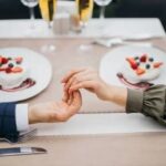 A close-up of a couple gently touching hands across a restaurant table during a date, demonstrating how to build attraction using subtle physical cues.