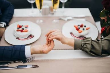 A close-up of a couple gently touching hands across a restaurant table during a date, demonstrating how to build attraction using subtle physical cues.