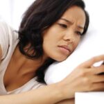 A close-up shot of a young woman looking at her smartphone with a disappointed expression, learning how to handle rejection after receiving a tough text message.