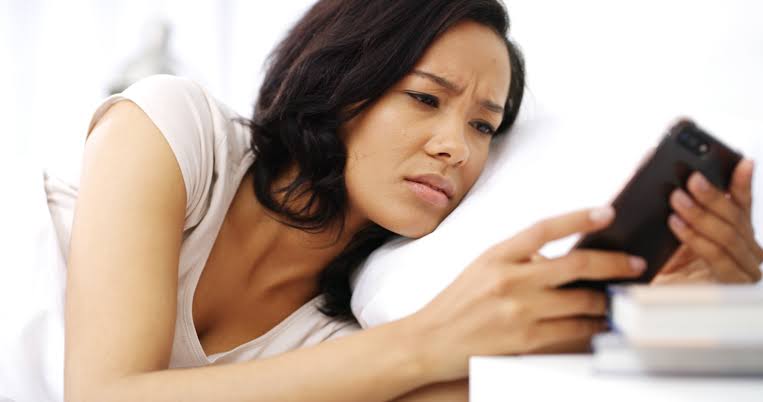 A close-up shot of a young woman looking at her smartphone with a disappointed expression, learning how to handle rejection after receiving a tough text message.