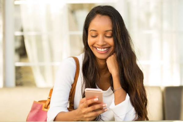 A young woman smiling warmly while checking her smartphone to decide what to do after the first date.
